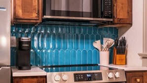 Une cuisine avec des meubles en bois, un four à micro-ondes en acier inoxydable, une cuisinière et un dosseret de carrelage bleu.