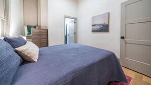 Une chambre à coucher avec un lit, une commode, une porte et un tableau accroché au mur.