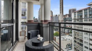 A balcony with a wicker table and chairs, a potted plant, and a view of surrounding buildings. - Heart of the City Apartment (Auckland)