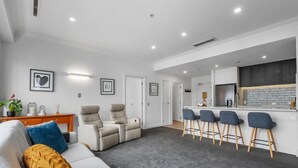 A modern living room with a sofa, chairs, and a bar area with stools. - Heart of the City Apartment (Auckland)