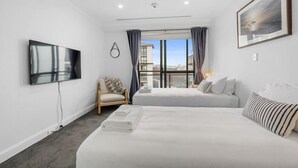 A hotel room with a large bed, a smaller bed, a TV mounted on the wall, a chair, and a window with curtains. - Heart of the City Apartment (Auckland)