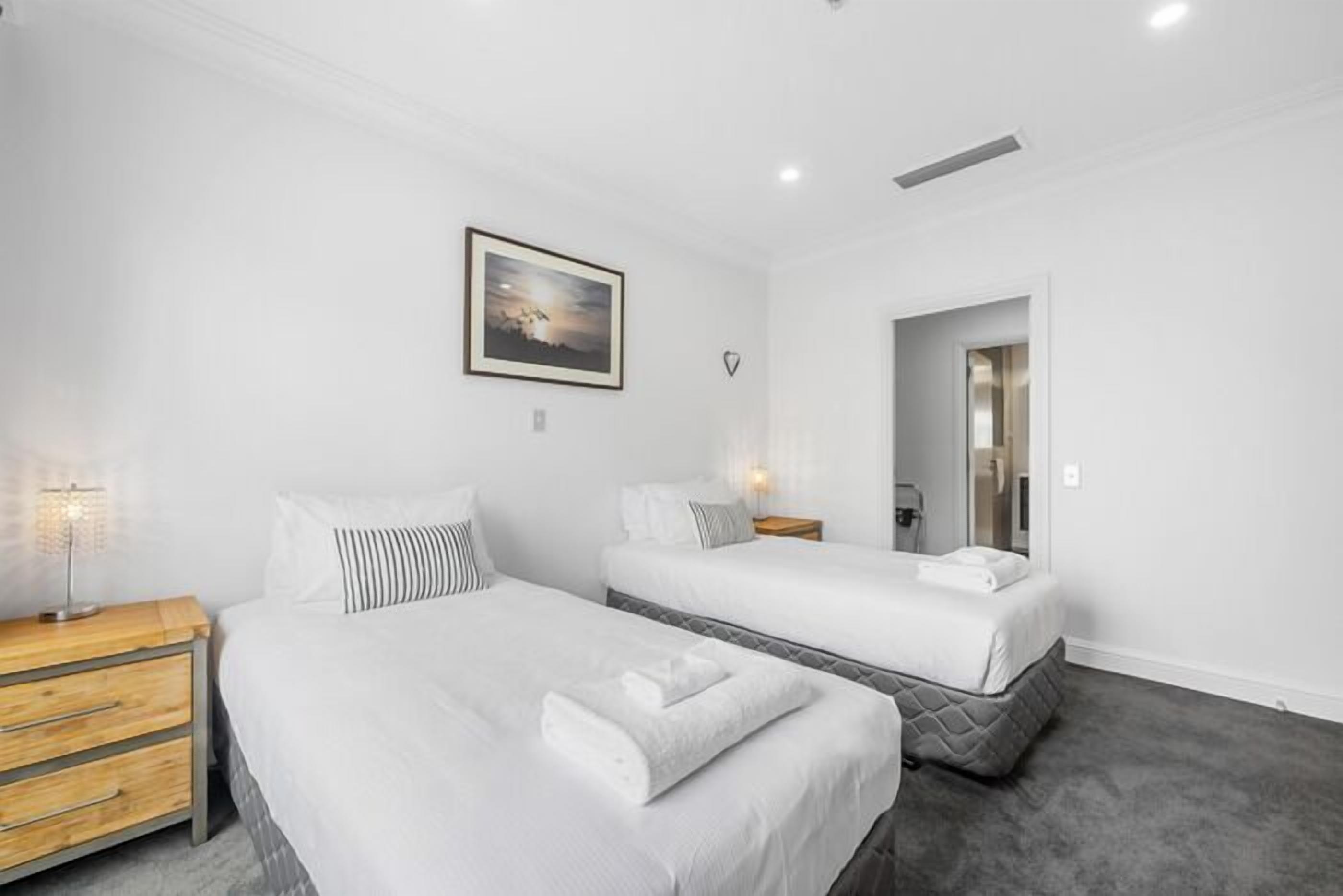 A hotel room with two beds, a wooden nightstand, a framed picture on the wall, and a mirror in the corner.