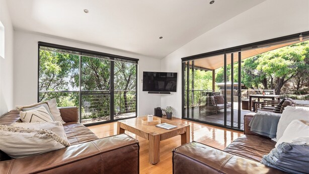 Un salon moderne avec des canapés en cuir, une table basse en bois et de grandes portes-fenêtres coulissantes donnant sur une terrasse extérieure.
