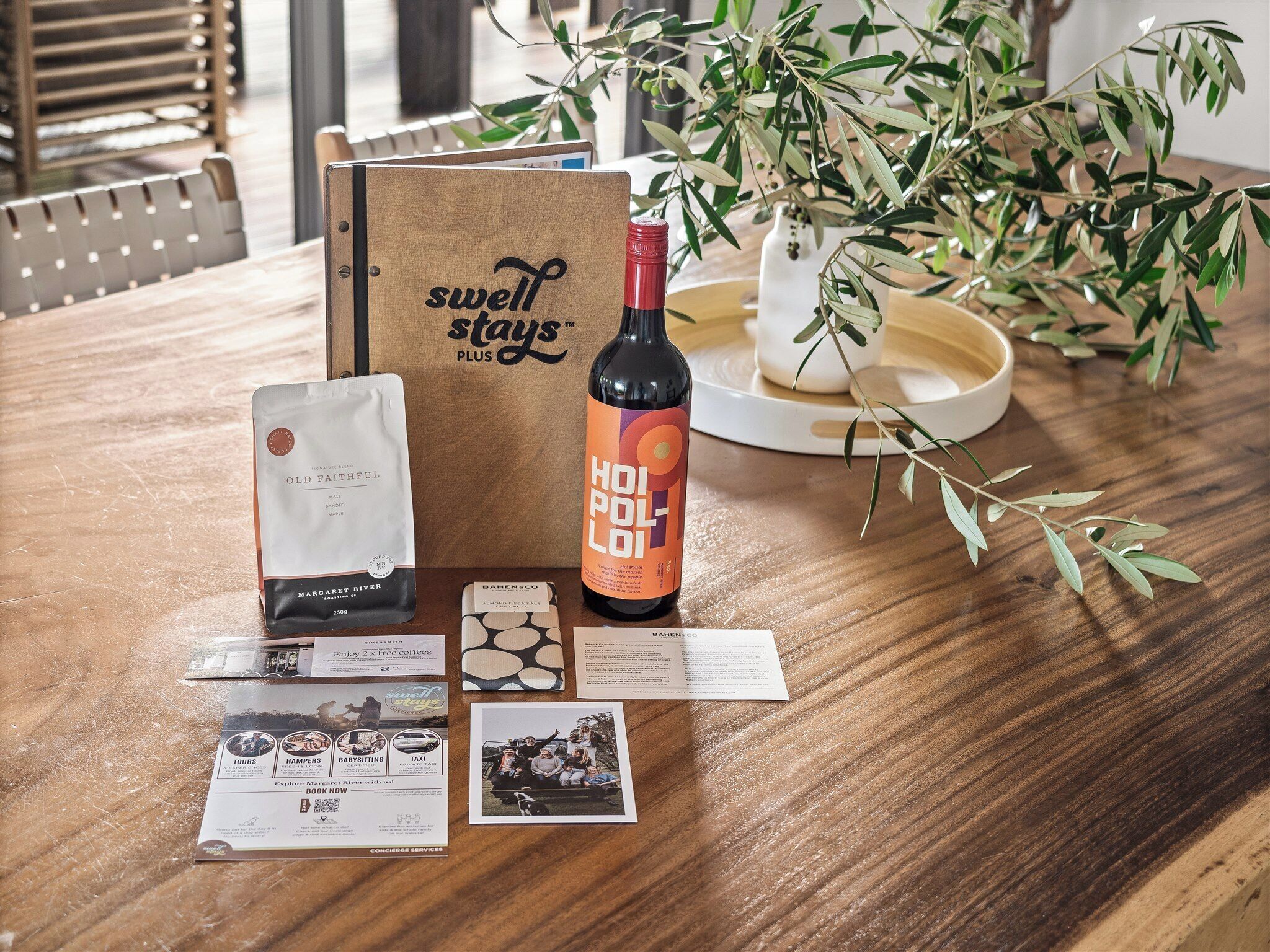 Un tavolo di legno con una bottiglia di vino, una confezione di caffè, una tessera e un depliant.