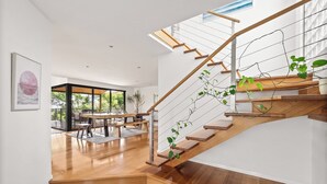 Un escalier moderne avec des marches en bois et des rampes en métal, menant à un balcon d’où l’on peut admirer la verdure.