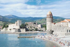 A coastal town with historic stone buildings, a prominent tower, and a beach area with people and boats. - La Bergerie, tranquil retreat with pool in its own valley 30 miles from the sea (Montferrer)