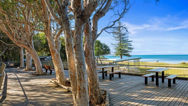 A wooden deck with picnic tables overlooking a beach.