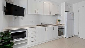 A modern kitchen with white cabinetry, a built-in microwave, a stainless steel sink, and a refrigerator.