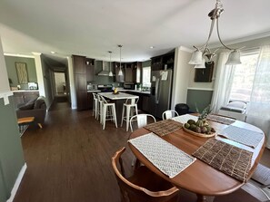Cozinha moderna com ilha central, banquetas brancas e mesa de jantar com jogos americanos.