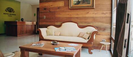 Vestíbulo con suelo de madera, una recepción, un sofá y una mesa baja con revistas.
