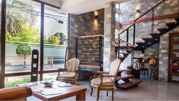 A spacious room with a large window, a stone wall, a wooden staircase, and a dining area with chairs and a table. - Hotel Madero Talca (Talca)