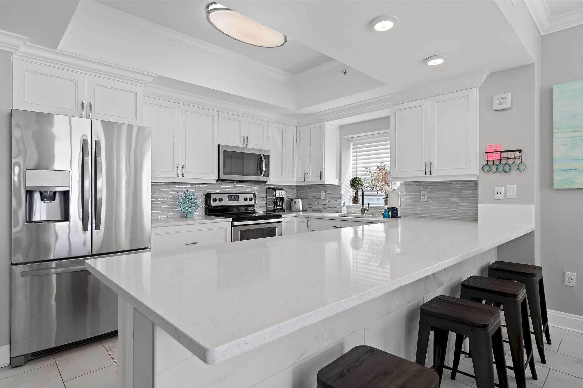 A modern kitchen with white cabinetry, stainless steel appliances, a large island with bar stools, and a window with blinds.