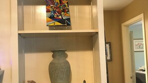Ein mehrstufiges Regal mit verschiedenen dekorativen Elementen, darunter eine Buddha-Statue, eine Vase und ein farbenfrohes Gemälde.