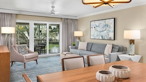 Habitación de hotel con sofá, sillón, mesa de comedor y un balcón con vistas a zonas verdes.