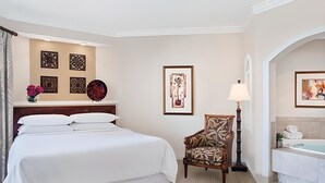 Habitación de hotel con una cama grande, una silla, un escritorio, una lámpara y un baño con bañera y toallas.