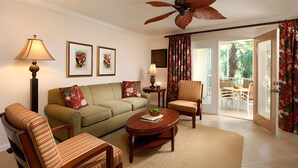 Una sala de estar con un sofá, sillones, una mesa de centro y un ventilador de techo. Hay cuadros enmarcados en la pared y vistas al exterior a través de una puerta.