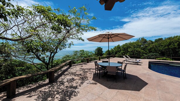 Une terrasse extérieure avec une piscine, entourée d’arbres et offrant une vue dégagée sur l’océan.