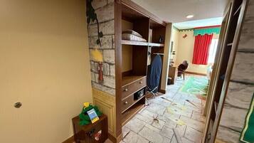 A hotel room with a stone wall, a wooden wardrobe, a desk, and a red curtain.