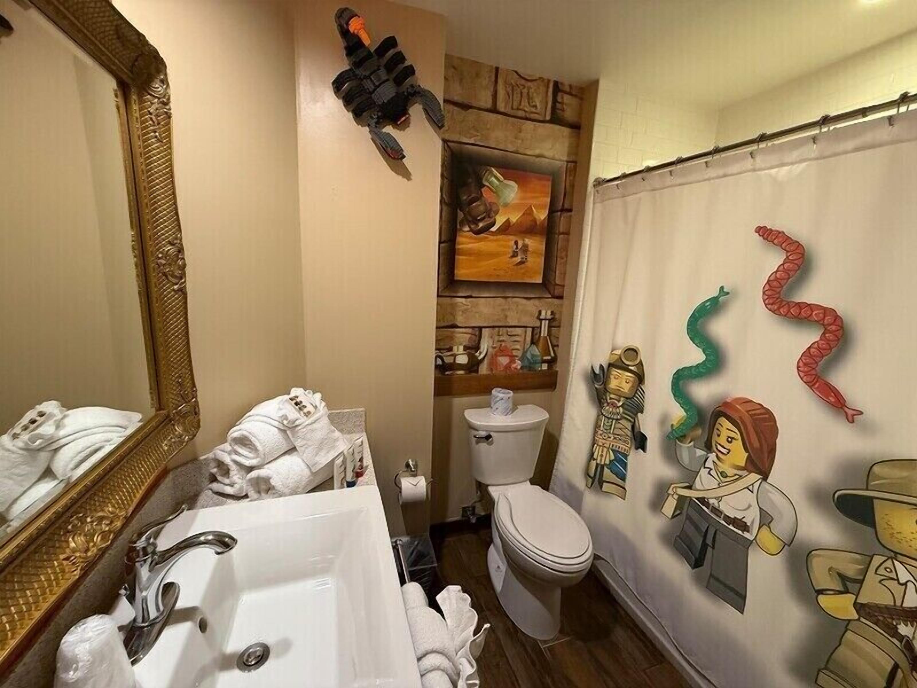 Une salle de bain avec un grand miroir, un lavabo, des toilettes et un rideau de douche orné de personnages de dessins animés.