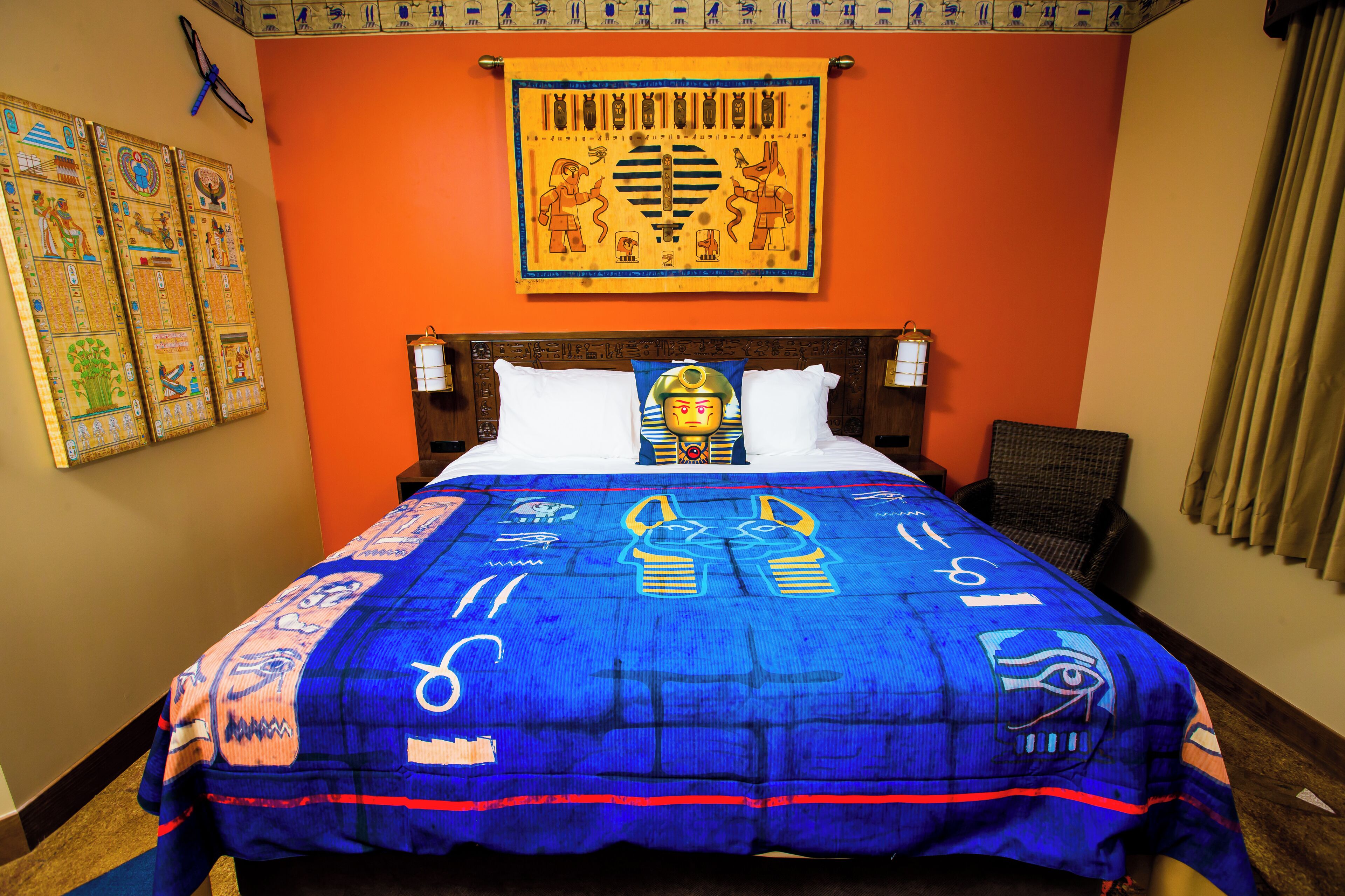 A hotel room with an Egyptian-themed bedspread, a wall with Egyptian wall art, and a bed with white pillows.