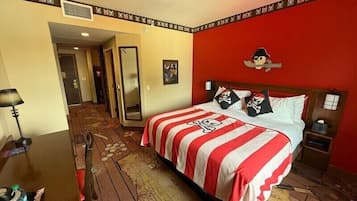 A hotel room with a large bed, a wooden floor, a red accent wall, and a pirate-themed bedspread.