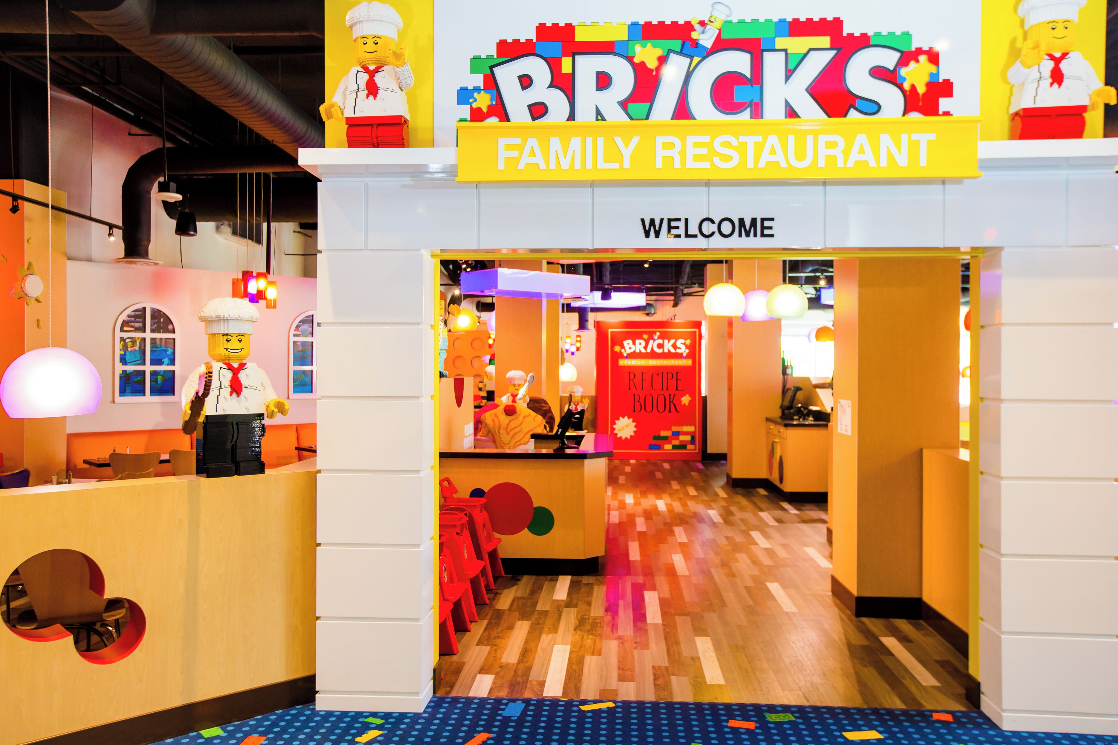 El interior de un restaurante con temática de LEGO, con un cartel de 'Welcome', decoraciones de personajes de LEGO y un diseño de suelo colorido.