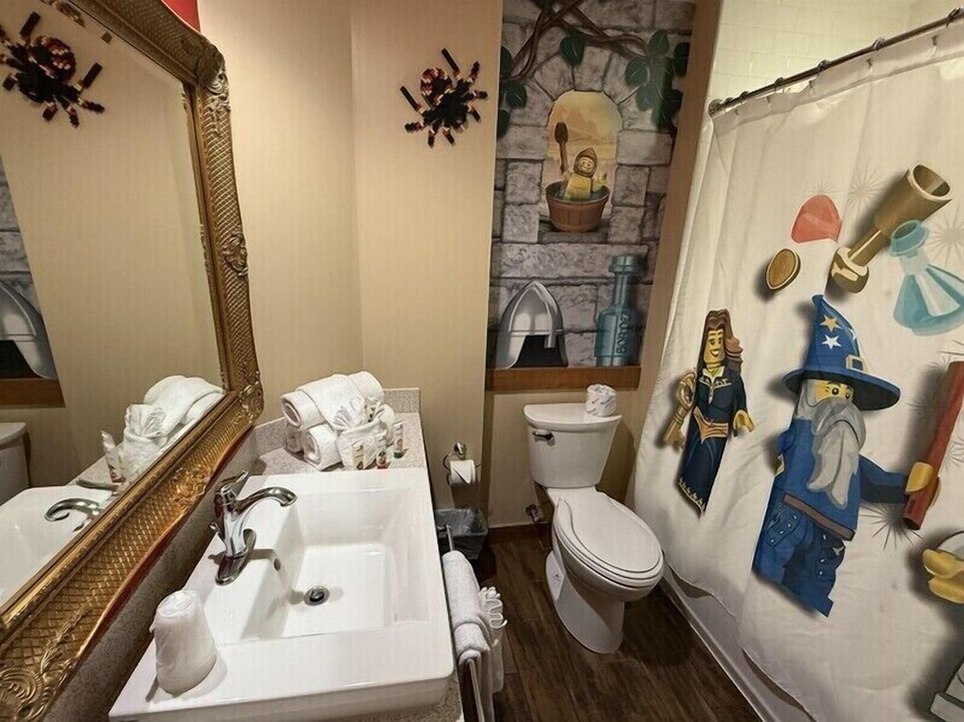 Une salle de bain avec un grand miroir, un lavabo, des toilettes et un rideau de douche orné de personnages de dessins animés.