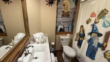 Une salle de bain avec un grand miroir, un lavabo, des toilettes et un rideau de douche orné de personnages de dessins animés.
