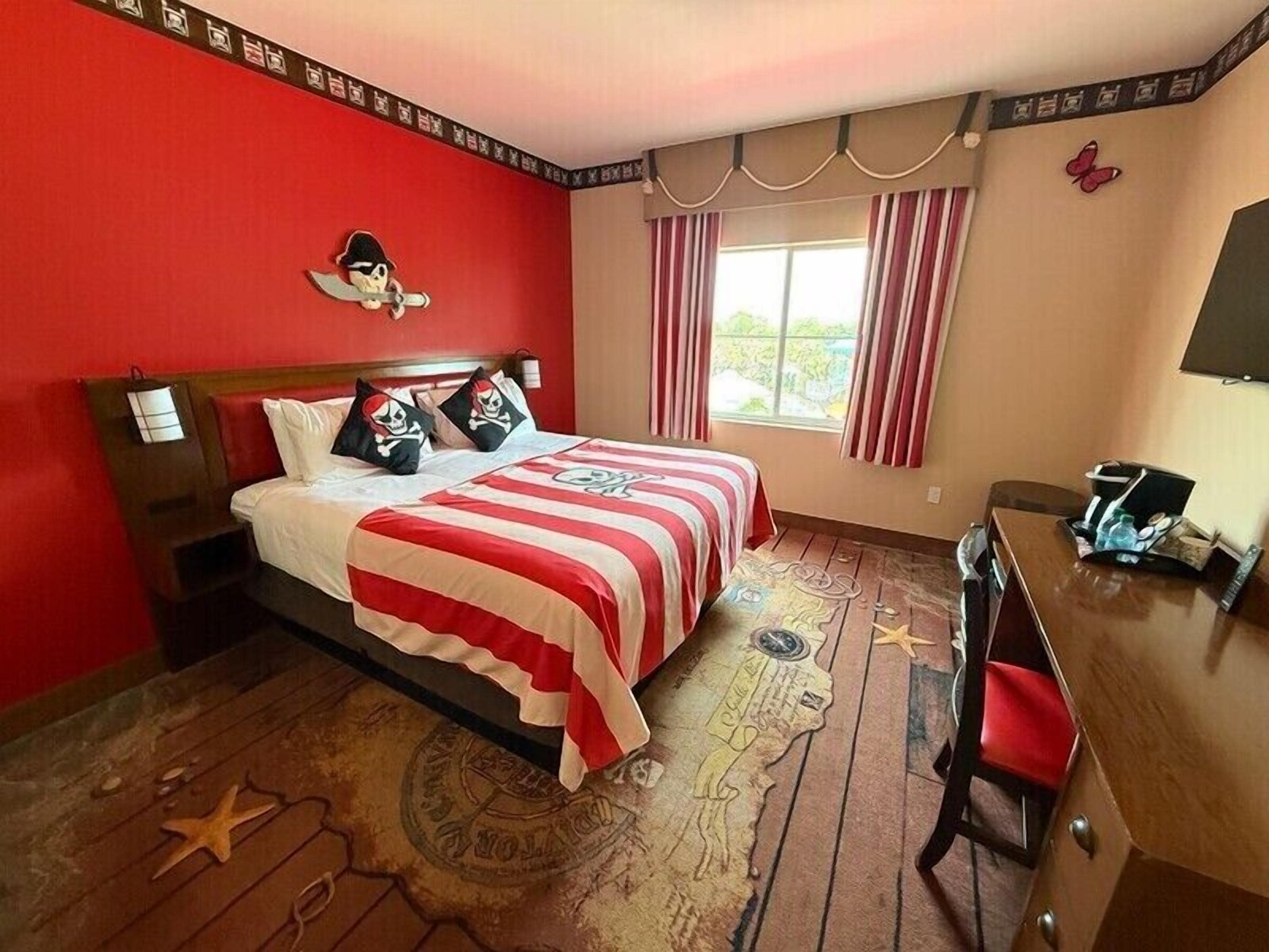 A hotel room with a red and white striped bedspread, a skull and crossbones pillow, and a starfish decoration on the floor.