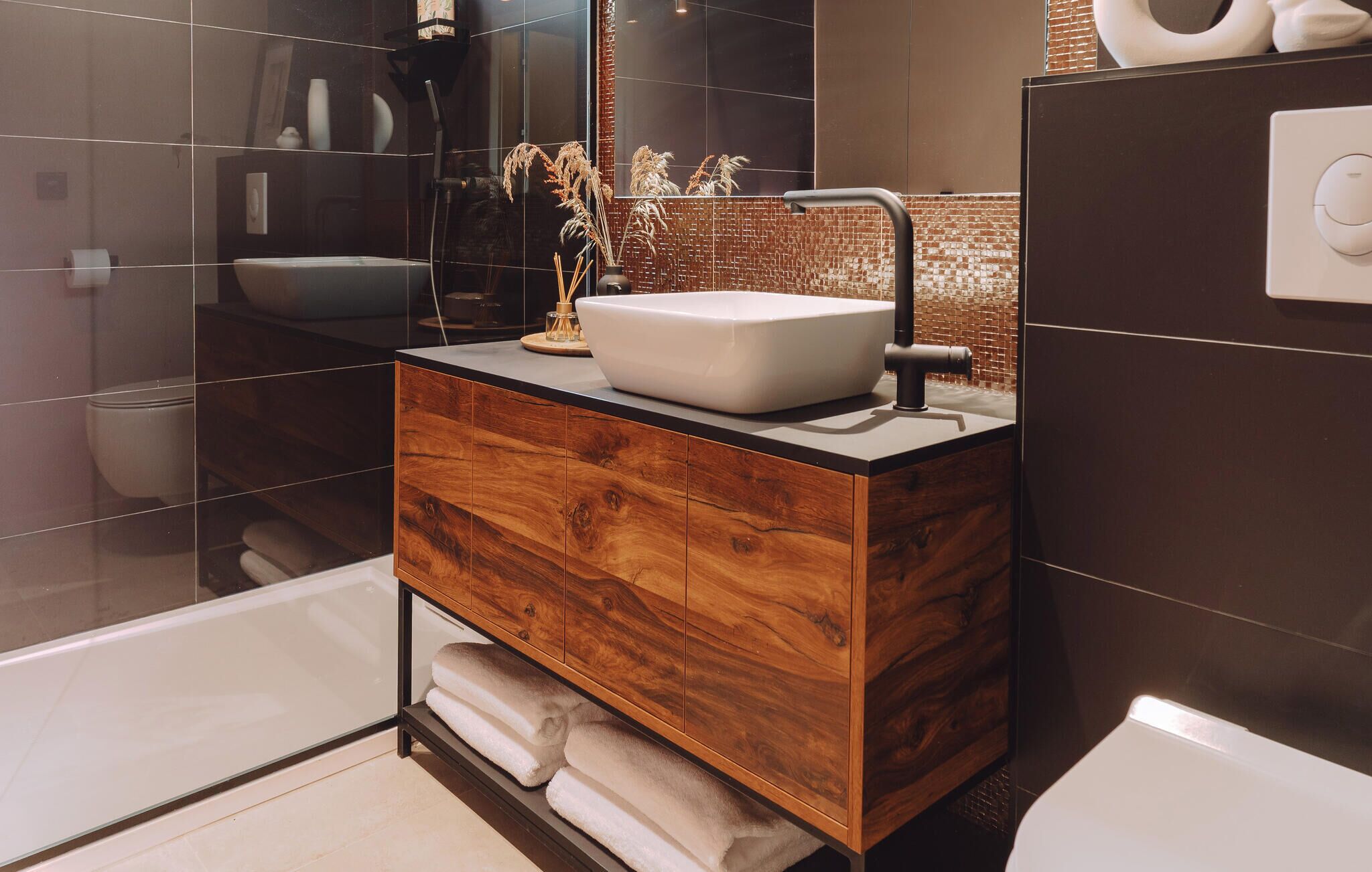 A modern bathroom with a wooden vanity, a white sink, and a glass shower enclosure.