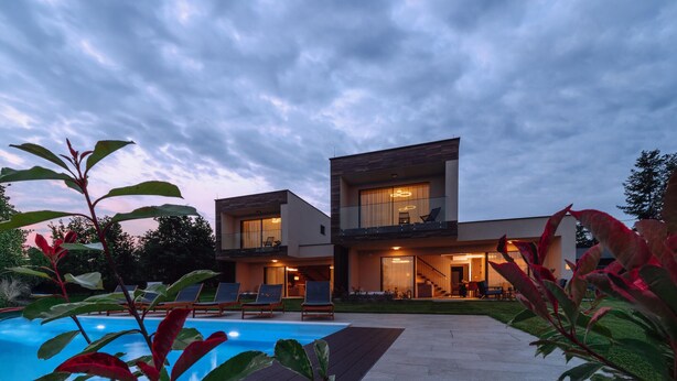 Une maison moderne à deux étages, dotée d’une piscine, d’un espace salon extérieur et d’une grande fenêtre.