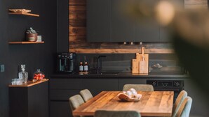 Une cuisine moderne avec des meubles de couleur sombre, un plan de travail en bois, une machine à café et un coin repas comprenant une table et des chaises en bois.