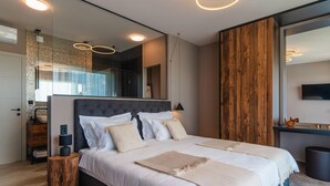 Une chambre à coucher moderne avec un grand lit, une tête de lit en bois, un miroir et un téléviseur fixé au mur.