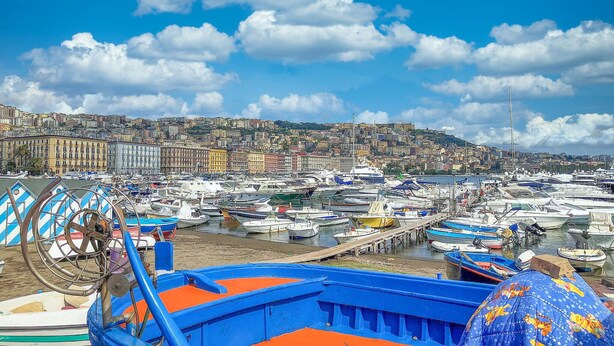 Un puerto deportivo lleno de barcos, con un paisaje urbano al fondo y un cielo azul despejado.