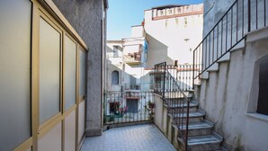 Un estrecho callejón con suelo de baldosas, una escalera de metal y un edificio con un balcón.