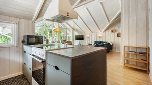 A modern kitchen with a central island, a dining area with a sofa, and a TV mounted on the wall.
