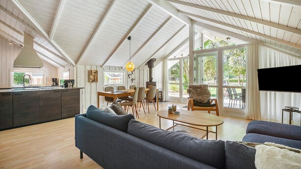 A spacious living area with a high ceiling, a dining table, sofas, and a kitchen area with a sink and coffee machine.