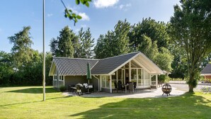 A house with a sloped roof, a covered patio with outdoor furniture, and a lawn.