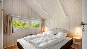 A bedroom with a bed, a window with curtains, a bedside lamp, and a wooden headboard.
