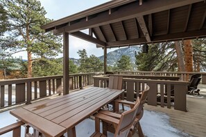 Una terraza de madera con una mesa y sillas, rodeada de árboles y vistas a la montaña.