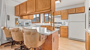 A modern kitchen with wooden cabinets, a central island with bar stools, a microwave, stove, and refrigerator. - Elkhorn West -Amazing views! Close to town! (Estes Park)