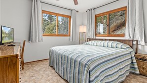 A bedroom with a bed, a desk with a computer, two windows with curtains, a lamp, and a view of trees. - Elkhorn West -Amazing views! Close to town! (Estes Park)