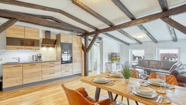 A modern kitchen with wooden cabinets, a built-in oven, and a dining area with a wooden table set for two.
