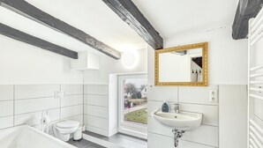A modern bathroom with a bathtub, toilet, and sink, featuring white tiles and exposed wooden beams.