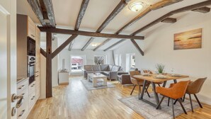 A spacious living area with a high ceiling and exposed wooden beams, a dining table set for four, and a view of the outside through large windows.