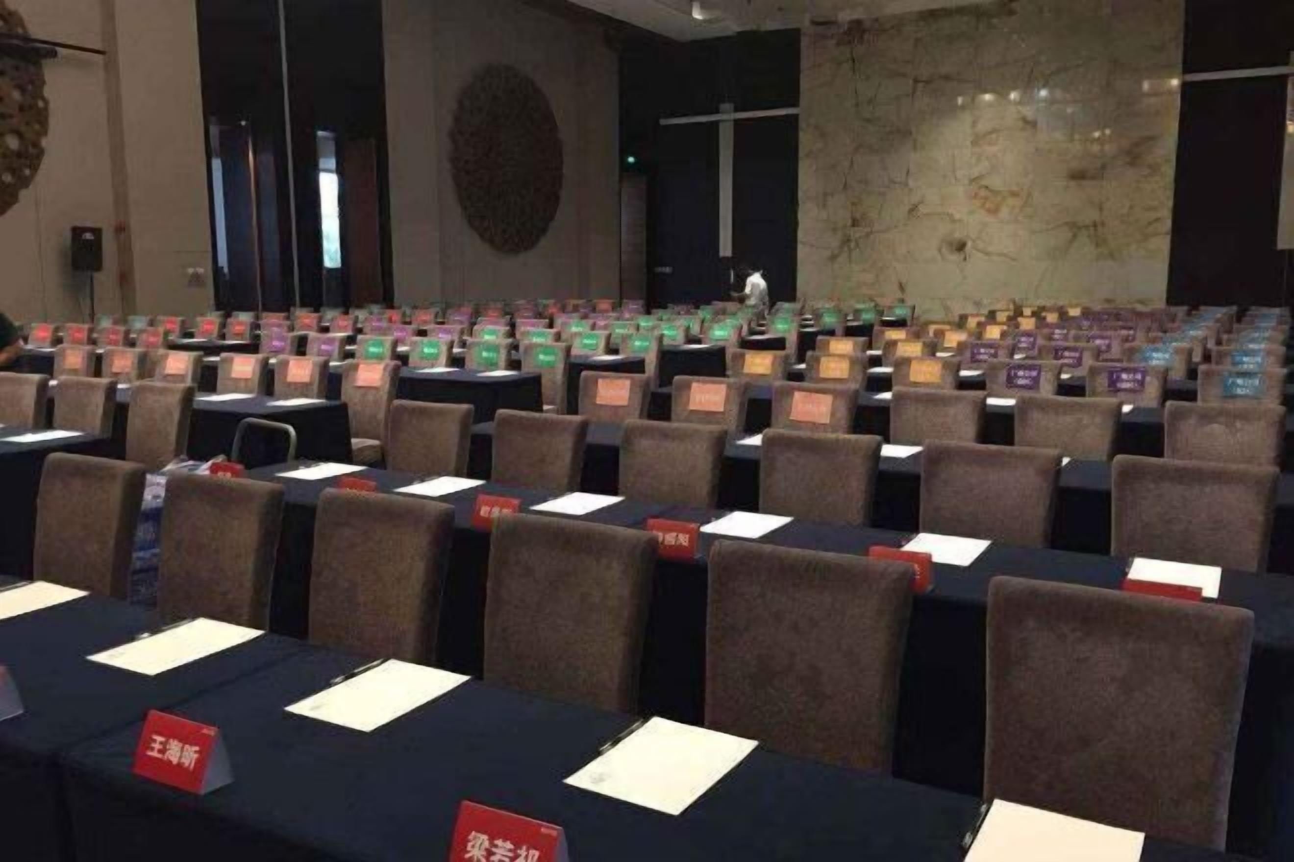A conference room with rows of tables and chairs, nameplates, and a stage.