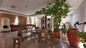 Un hall d’entrée spacieux, avec un banc en bois, une table ronde et un grand arbre en pot.