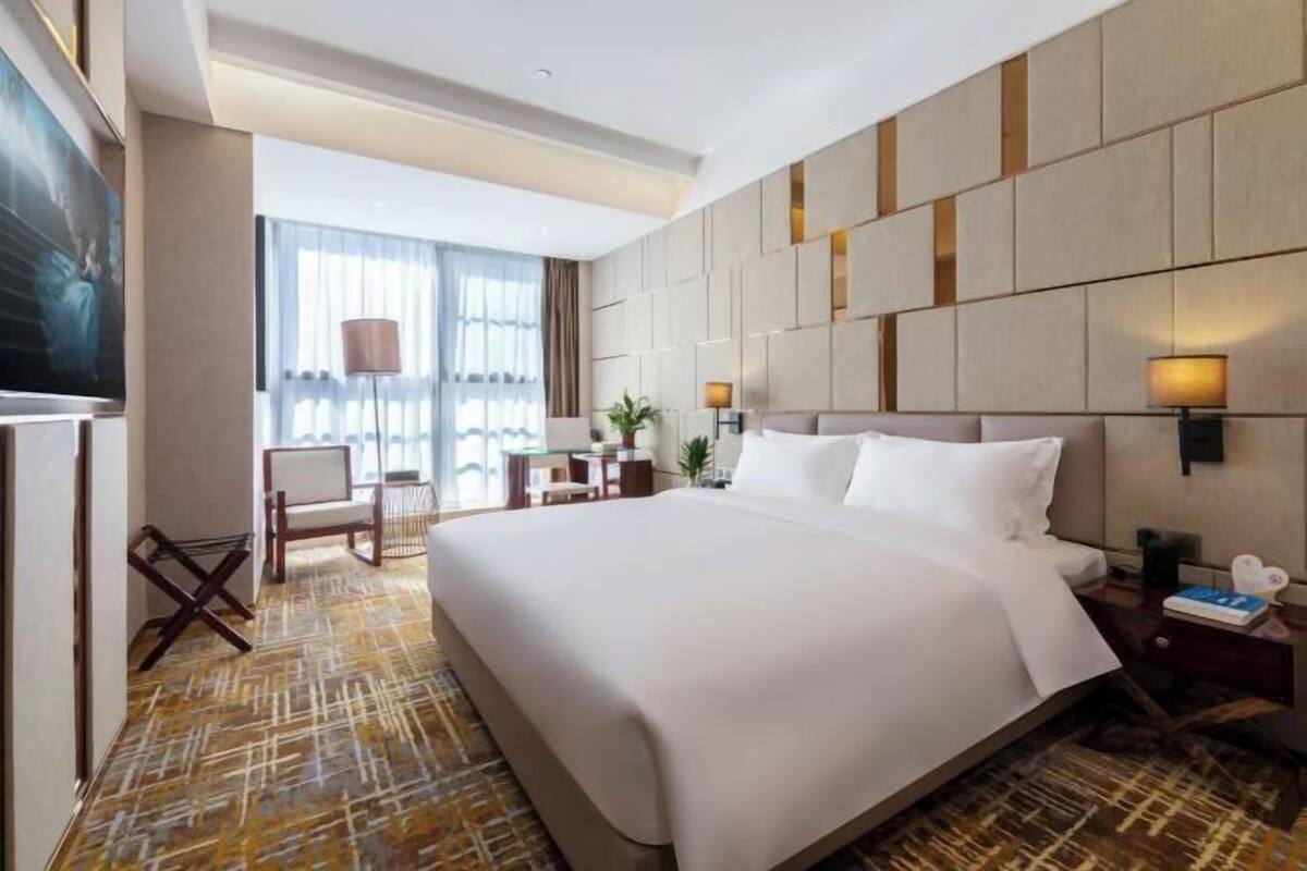 A hotel room with a large bed, a desk, a chair, and a television.