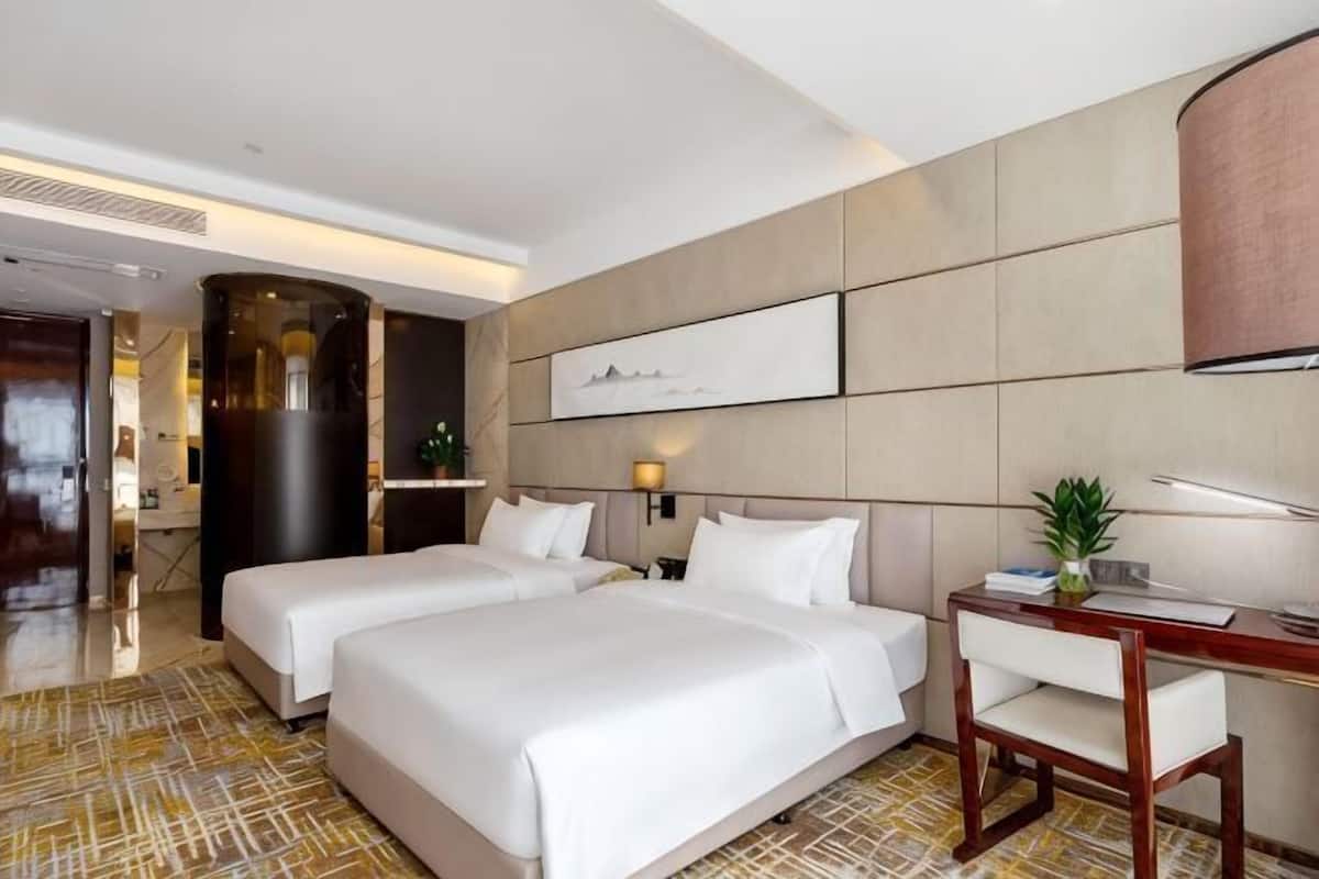 A hotel room with two beds, a desk, a chair, a lamp, and a large artwork on the wall.