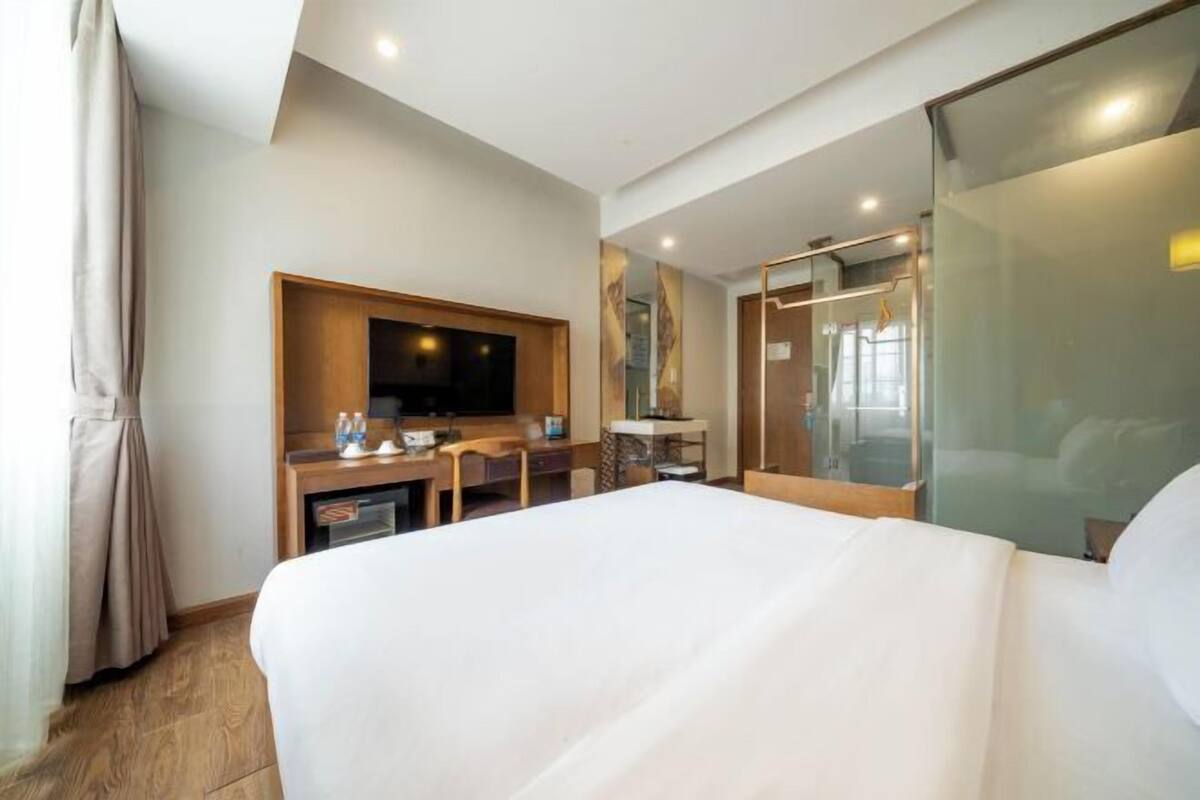A hotel room with a bed, a desk with a television, a mirror, and a sliding door.
